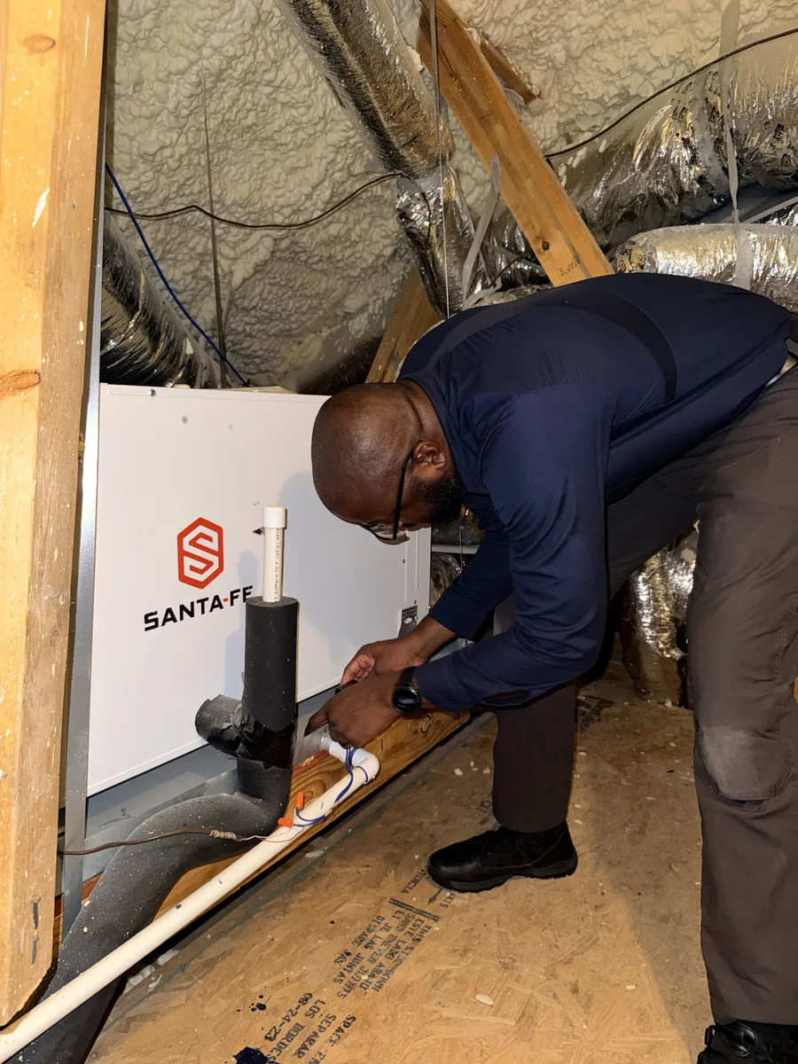 The technician connecting condensate drain lines to a whole-home dehumidifier installed in an attic.